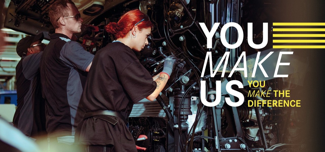 Young employees assemble parts on a truck in Daimler Truck Production - teamwork and commitment in a holiday job. Text in the picture: ‘You make us - You make the difference.’
